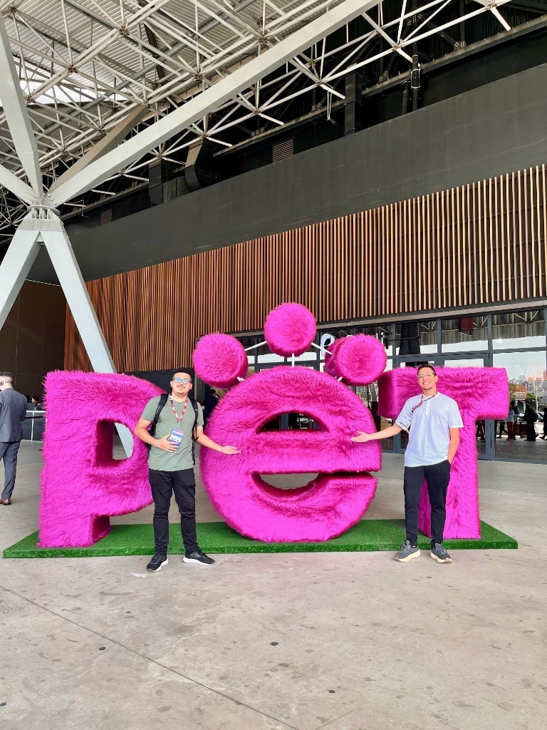João à esquerda (Filmmaker da Veler) e Vinícius à direita (Founder da Veler) ao lado do letreiro PET na PETSA 2026, no Distrito Anhembi em São Paulo